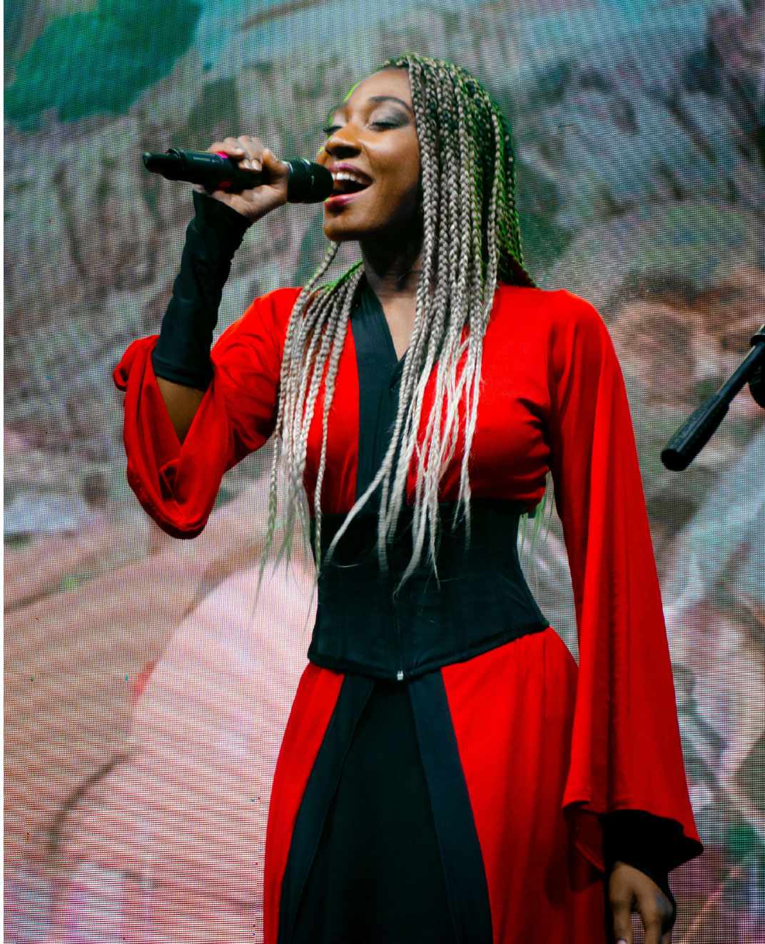 A person with long braids sings into a microphone